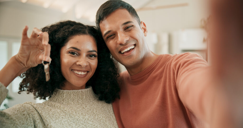 Um casal está tirando uma selfie e comemorando a conquista das chaves de sua nova casa. Seus sorrisos refletem felicidade e empolgação por esse marco importante em suas vidas.