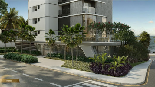 Fachada de edifício com jardim elevado, palmeiras e acesso por calçada arborizada junto ao mar.