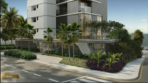 Entrada de edifício moderno com paisagismo, fachada de vidro e vista para o mar.