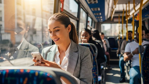 Mulher olhando o celular sentada próxima à janela em um ônibus urbano.