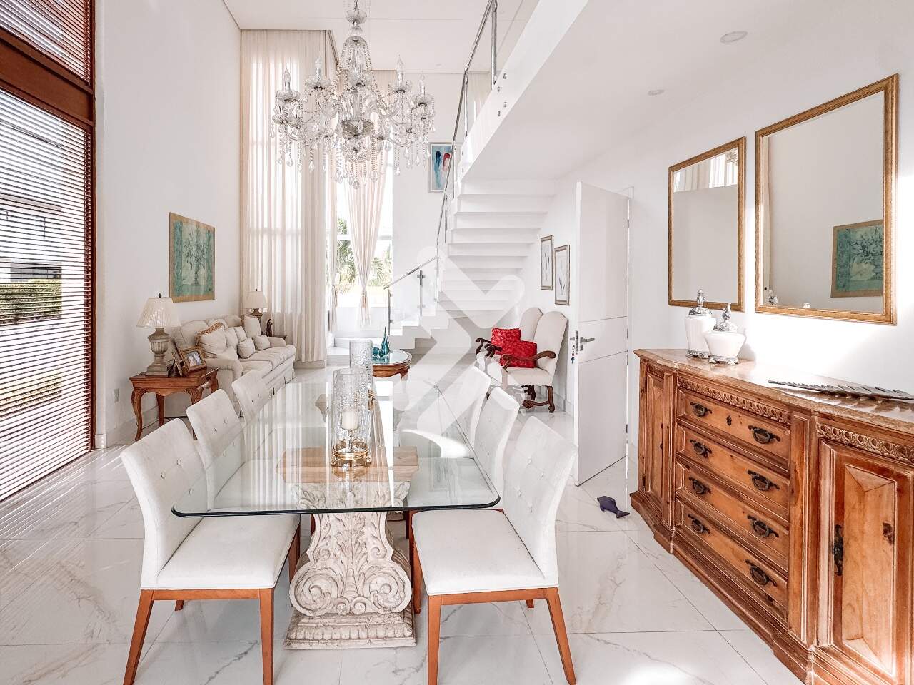 Imagem de uma sala de estar elegante e espaçosa com decoração sofisticada, destacando um lustre de cristal, móveis clássicos e janelas amplas, proporcionando uma sensação de conforto e luminosidade.
