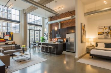 Um loft elegante com amplas janelas, um estilo industrial e móveis modernos. A sala de estar, cozinha e área de descanso são integradas, criando um ambiente acolhedor e aberto.